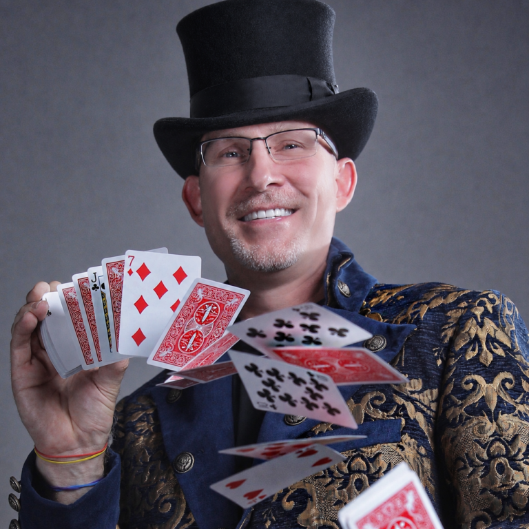 Danger Magic in a navy and gold jacket and top hat spraying a deck of cards