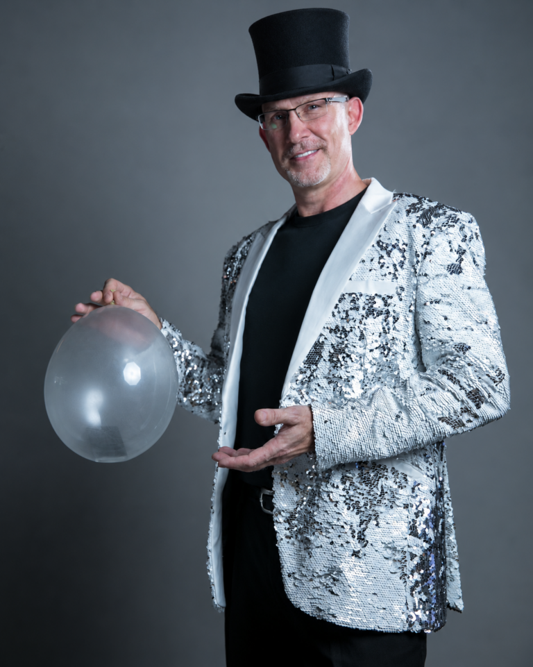 Danger Magic in a silver sequin jacket and top hat performing a phone-to-balloon effect